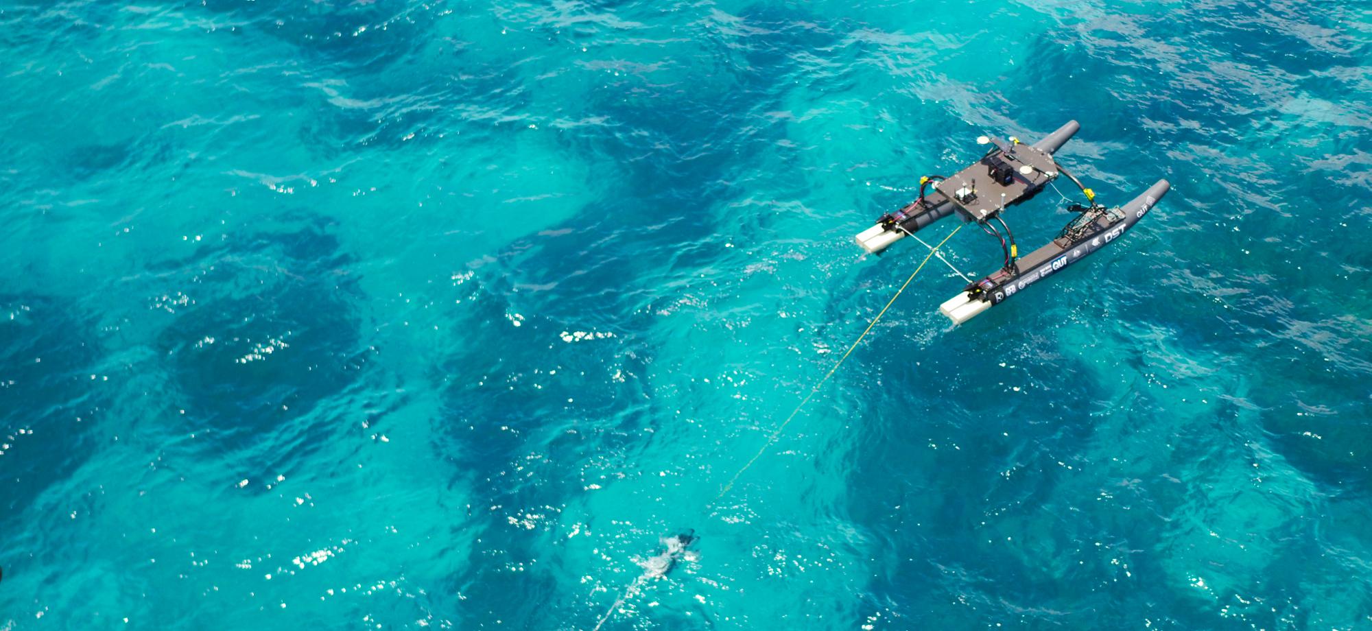 aerial photo of a grey and black autonomous vessel on the surface of the water above a coral reef