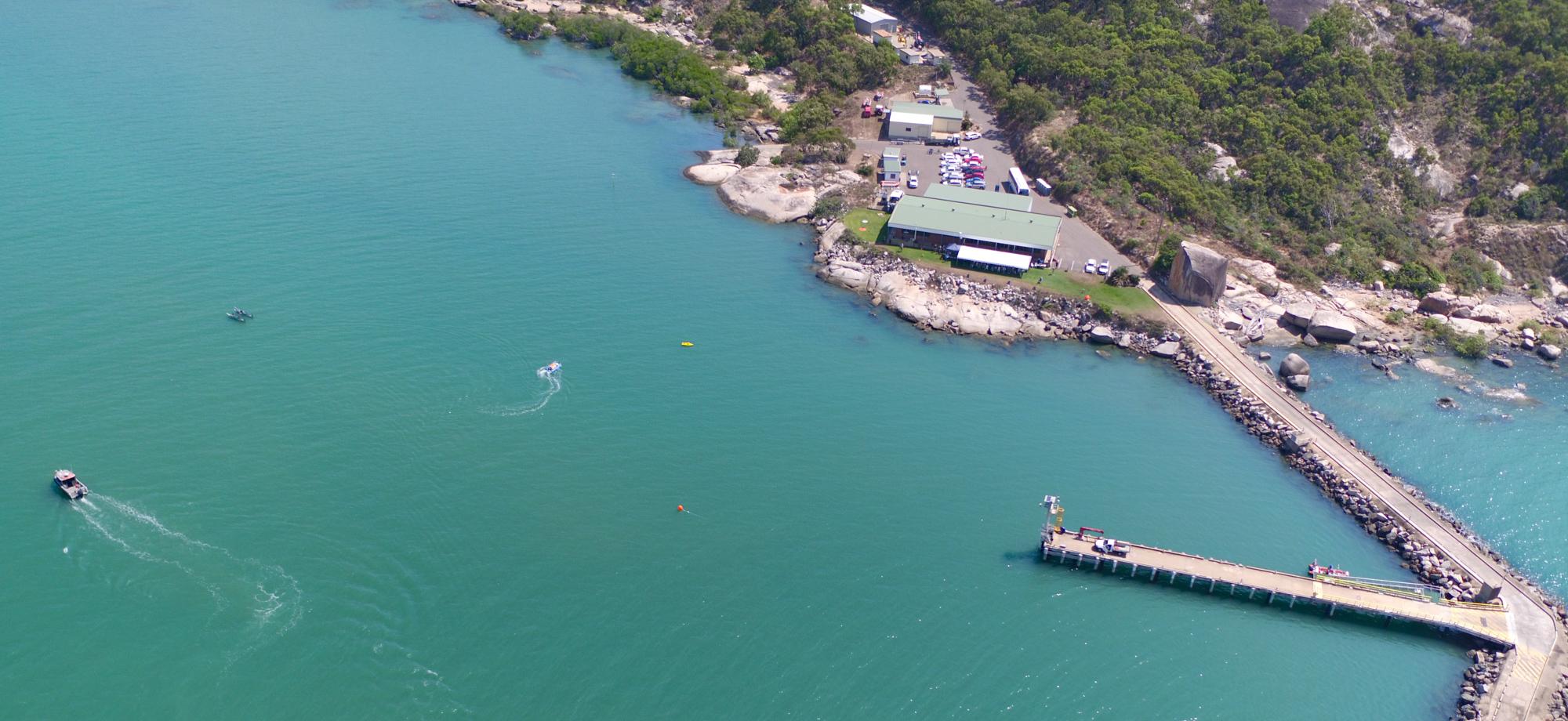 photo from a drone of shallow water and shoreline with a wharf connected to a building on land