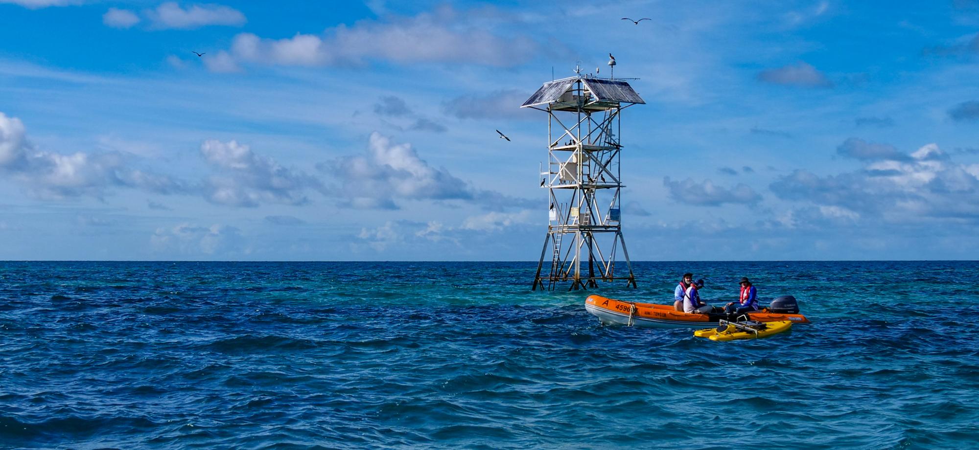 metal tower sticking up out of the ocean with a small boat and people in front of the tower