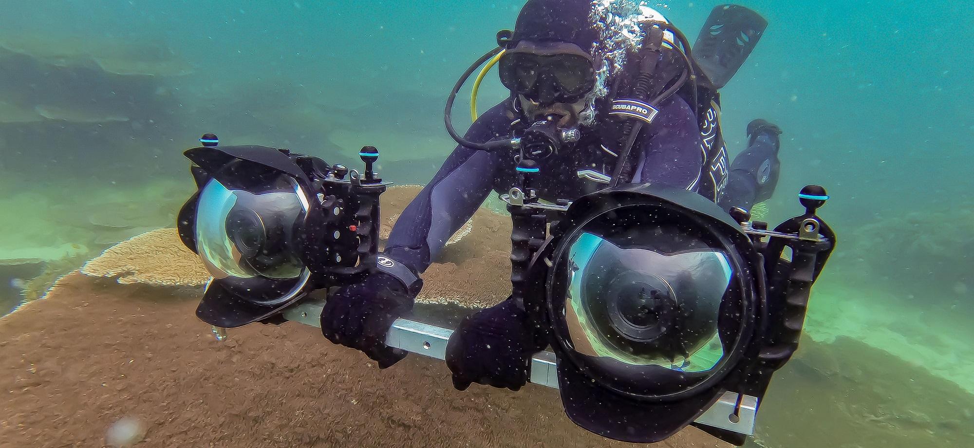 Scuba diver holds a bar with two large cameras on either end