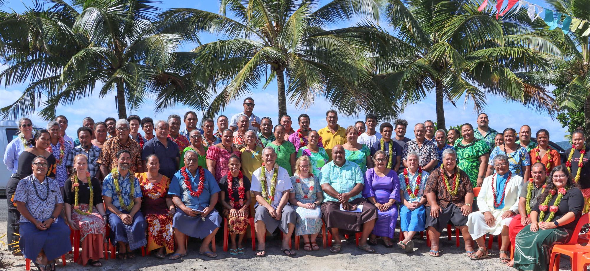 many people sitting in a group smiling at camera in front of palm trees