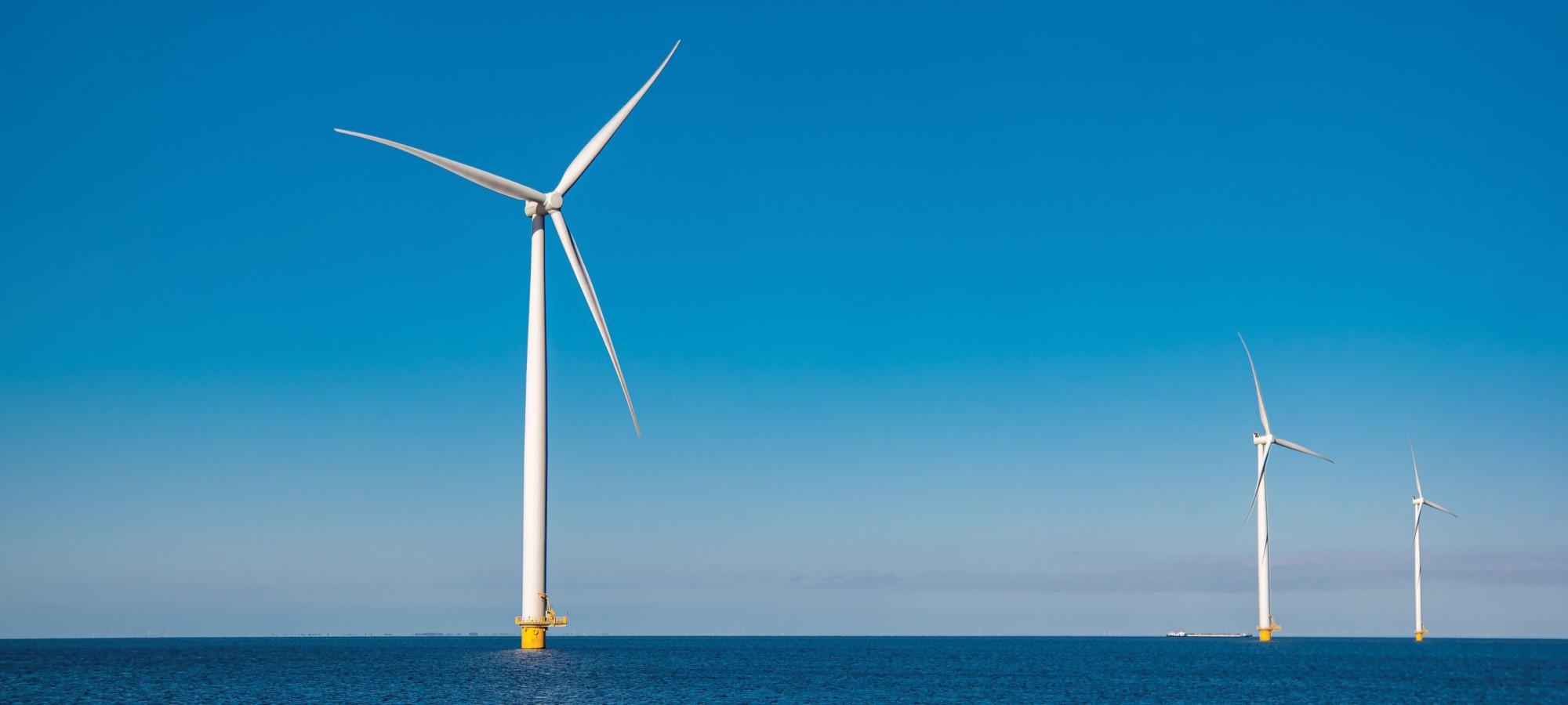 Three tall white windmills standing up out of an ocean scene with a clear sky