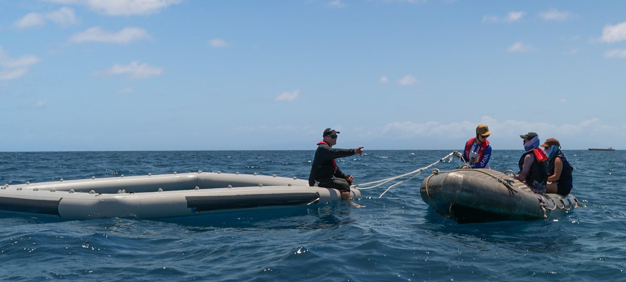 a number of people sitting on a small orange inflatable boat, next to a grey inflatable square
