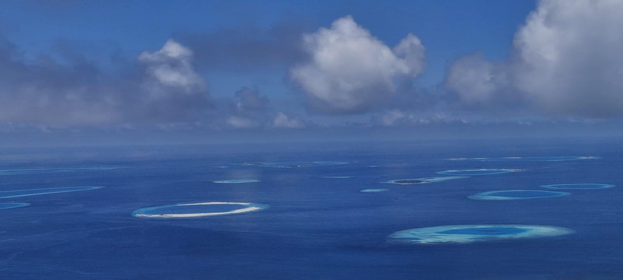 an aerial view of many reefs, with clouds above the ocean