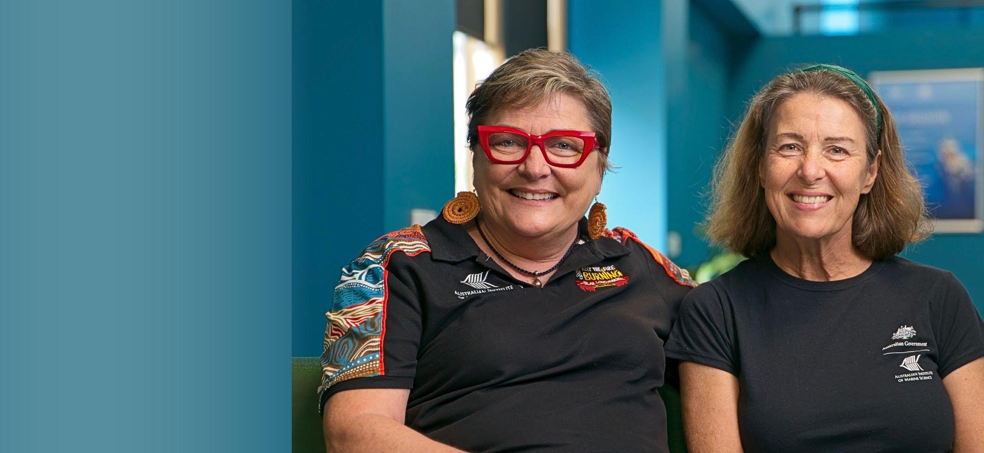 2 people sitting closely on a low couch and smiling at the camera