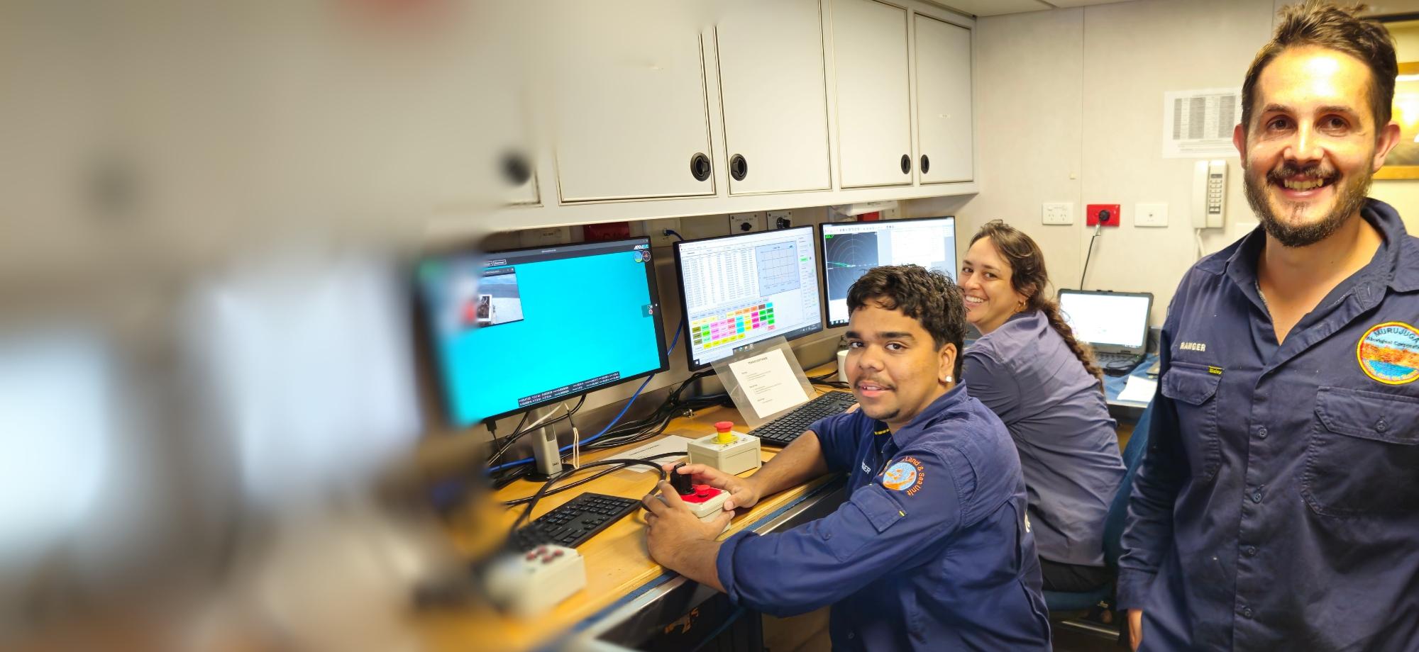 Three people posing in a control room of a science ship