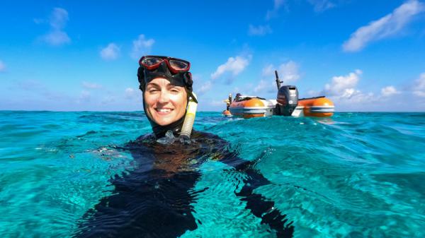 snorkeller in water smiling at camera with small bots in background