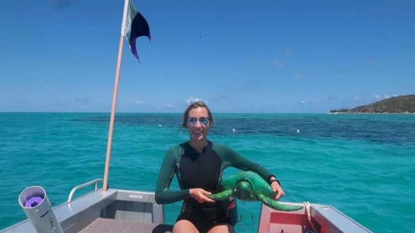 woman scientist on small vessel holding model of sea turtle