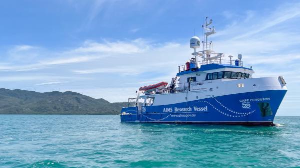 blue and white research vessel on a calm sea with island in background