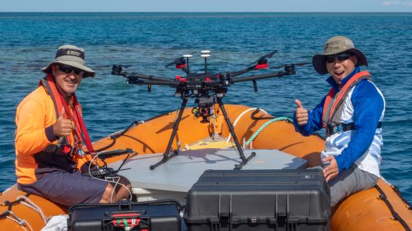 people in orange boat with a large drone