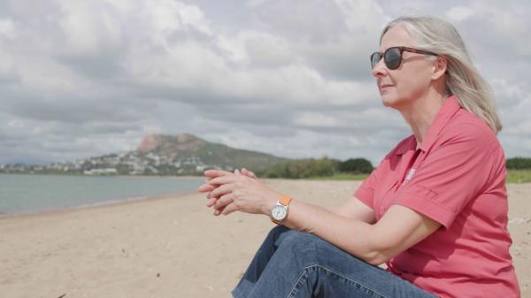 marine scientist sits on a beach with castle hill in townsville in the background