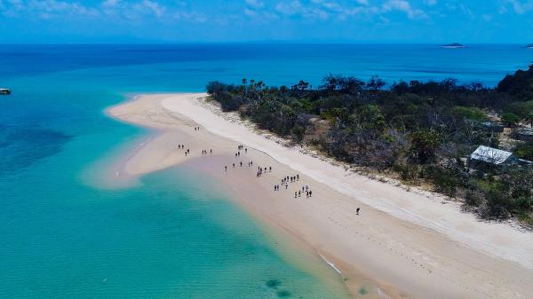 aerial view over white sand beach with people walking on it, next to a turquoise waters of the ocean