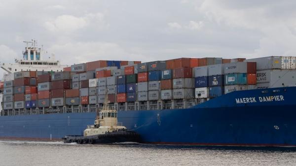 a cargo ship heads into port with two tug boats