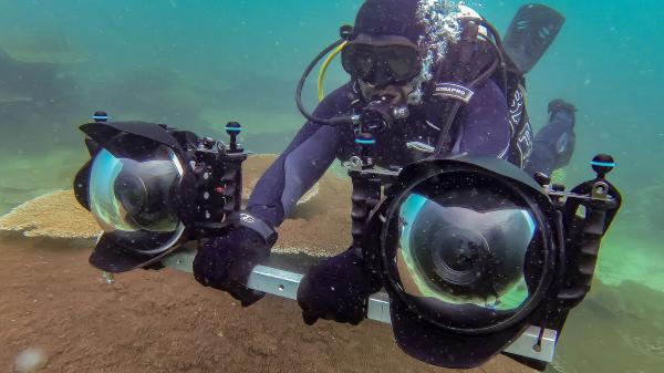 Scuba diver holds a bar with two large cameras on either end