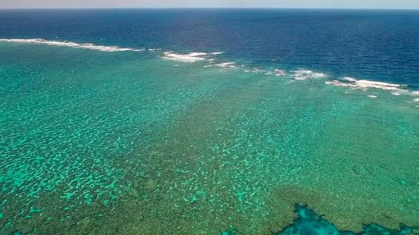 a birds eye view of a coral reef, with small waves breaking on the reef crest.