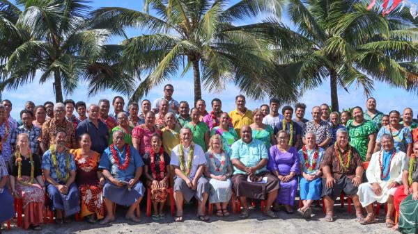 many people sitting in a group smiling at camera in front of palm trees