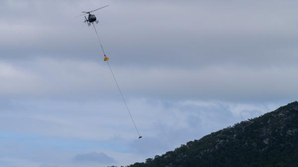 helicopter flies over a mountain with a cargo load hanging underneath