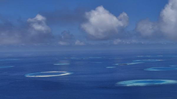 an aerial view of many reefs, with clouds above the ocean
