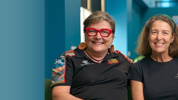 2 people sitting closely on a low couch and smiling at the camera