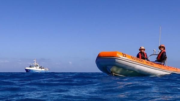 Marine scientists on a tender with research vessel in the background