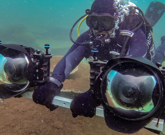 Scuba diver holds a bar with two large cameras on either end