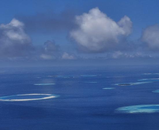 an aerial view of many reefs, with clouds above the ocean