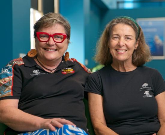 two women sitting on a couch together and smiling at the camera