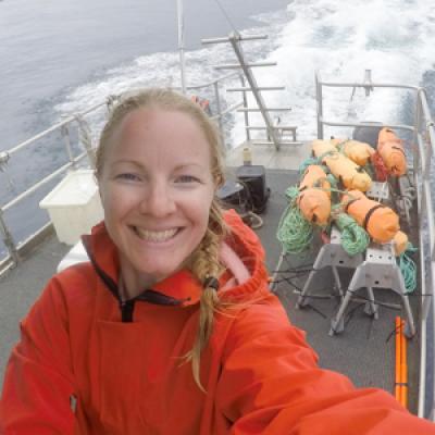 Woman wearing red jumper standing on back deck of boat.