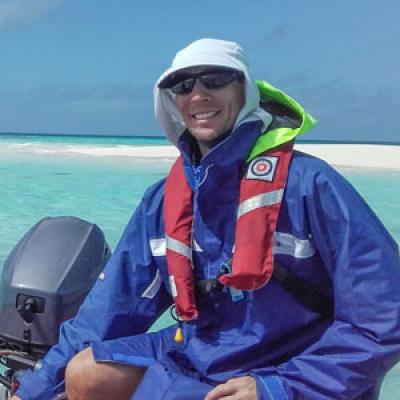 Man in sunglasses and hat smiling at camera while driving small boat