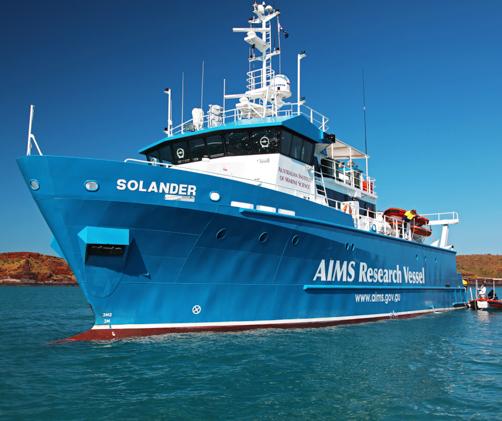 blue and white research vessel in front of red cliffs