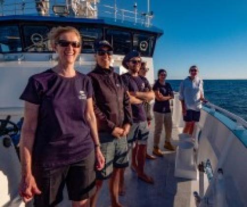 6 people standing on bow of large white vessel smiling at camera