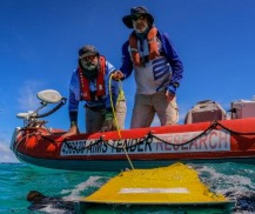 2 people on small boat holding a line to a yellow floating object in the water